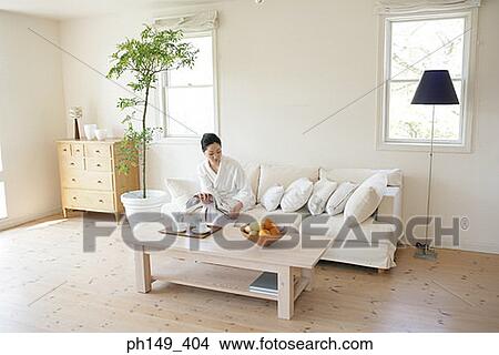 Young woman sitting on a couch and reading a magazine View Large Photo Image Picture - Young woman sitting on a couch and reading a magazine. Fotosearch