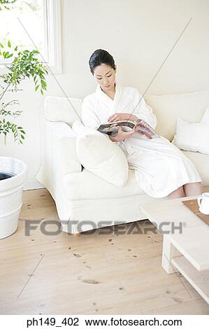Young woman sitting on a couch and reading a magazine View Large Photo Image Stock Image - Young woman sitting on a couch and reading a magazine. Fotosearch