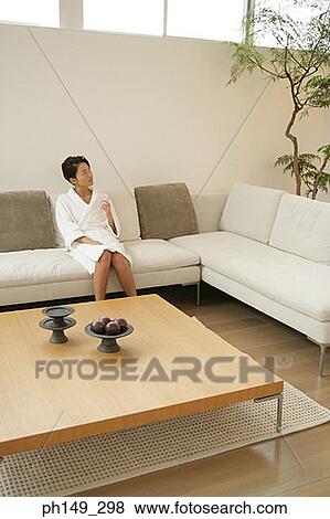 Young woman sitting on a couch and wearing a bathrobe View Large Photo Image Stock Photo - Young woman sitting on a couch and wearing a bathrobe. Fotosearch