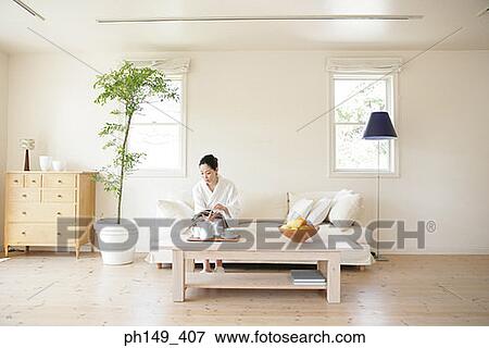 Young woman sitting on a couch and reading a magazine View Large Photo Image Stock Photo - Young woman sitting on a couch and reading a magazine. Fotosearch