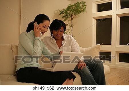 Young woman talking on a mobile phone and using a laptop with a young man sitting beside her View Large Photo Image Stock Image - Young woman talking on a mobile phone and using a laptop with a young man sitting beside her. Fotosearch