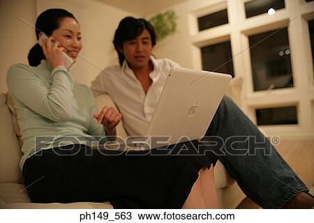 Young woman talking on a mobile phone and using a laptop with a young man sitting beside her View Large Photo Image Stock Image - Young woman talking on a mobile phone and using a laptop with a young man sitting beside her. Fotosearch