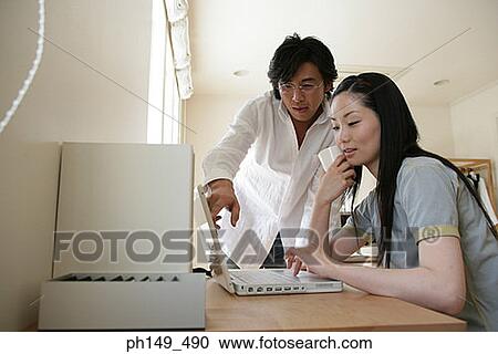 Young woman using a laptop with a young man pointing at the screen beside her View Large Photo Image Stock Image - Young woman using a laptop with a young man pointing at the screen beside her. Fotosearch
