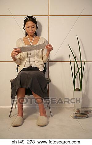 Young woman wearing headphones and reading a CD inlay card View Large Photo Image Stock Photo - Young woman wearing headphones and reading a CD inlay card. Fotosearch