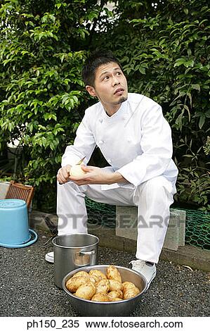 Stock Photography - Chef peeling raw potatoes in front of plants. Fotosearch