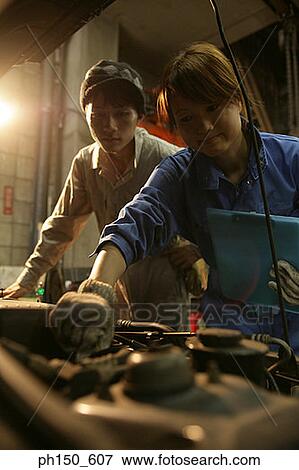 Close-up of a female auto mechanic examining an engine with another mechanic standing behind her View Large Photo Image Stock Photo - Close-up of a female auto mechanic examining an engine with another mechanic standing behind her. Fotosearch