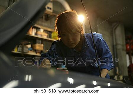Stock Photo - Close-up of a female auto mechanic examining an engine. Fotosearch