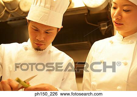 Stock Photograph - Close-up of a male chef cutting vegetable with a female chef looking at him. Fotosearch