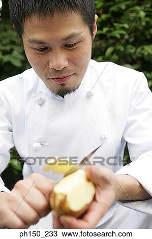 Stock Image - Close-up of a male chef peeling a raw potato. Fotosearch