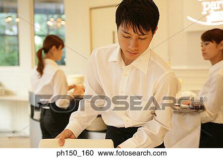 Close-up of a waiter arranging a chair with two waitresses standing behind him View Large Photo Image Stock Image - Close-up of a waiter arranging a chair with two waitresses standing behind him. Fotosearch