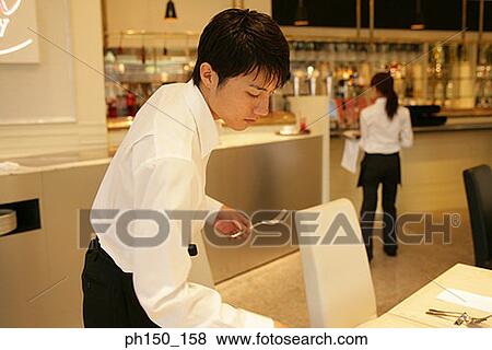 Stock Photo - Close-up of a waiter arranging a table with a waitress standing in the background. Fotosearch