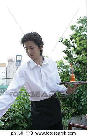 Stock Photo - Close-up of a waiter holding a serving tray and looking down. Fotosearch