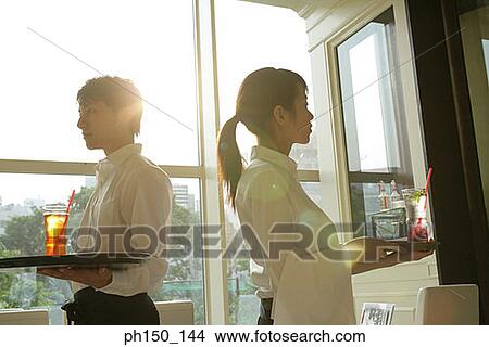 Close-up of a waiter standing with a waitress and holding trays View Large Photo Image Picture - Close-up of a waiter standing with a waitress and holding trays. Fotosearch