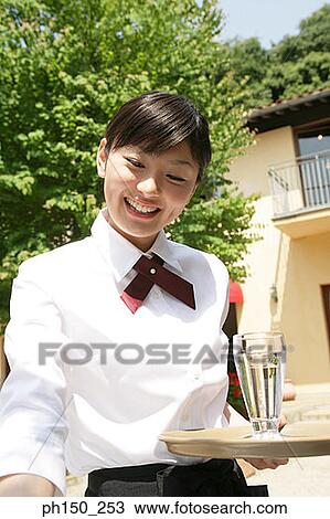 Stock Image - Close-up of a waitress holding a glass of water on a serving tray and smiling. Fotosearch