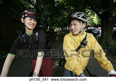 Stock Image - Close-up of a young couple walking with their bicycles and looking at each other. Fotosearch
