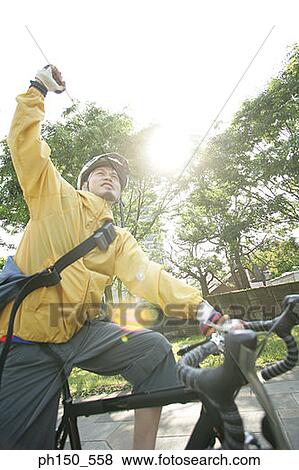 Close-up of a young man riding a bicycle with his hand raised View Large Photo Image Stock Photo - Close-up of a young man riding a bicycle with his hand raised. Fotosearch