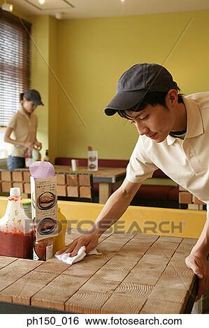 Close-up of a young man wiping a table with a napkin View Large Photo Image Stock Photograph - Close-up of a young man wiping a table with a napkin. Fotosearch