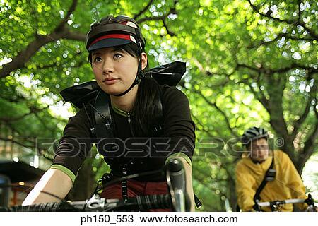 Stock Image - Close-up of a young woman riding a bicycle with a young man cycling in the background. Fotosearch