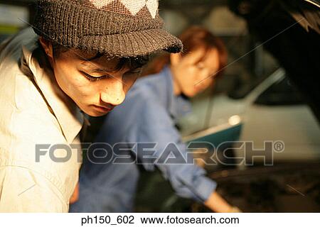 Close-up of an auto mechanic looking down with a female mechanic in the background View Large Photo Image Stock Image - Close-up of an auto mechanic looking down with a female mechanic in the background. Fotosearch