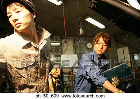 Close-up of two auto mechanics standing in front of a car View Large Photo Image Stock Photo - Close-up of two auto mechanics standing in front of a car. Fotosearch