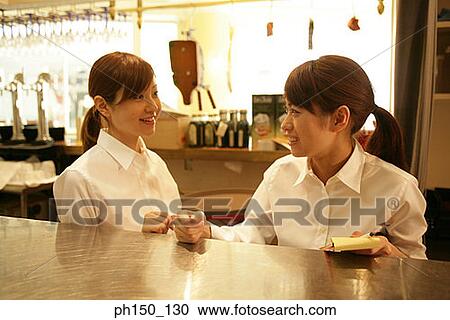 Stock Image - Close-up of two waitresses standing at a kitchen counter. Fotosearch