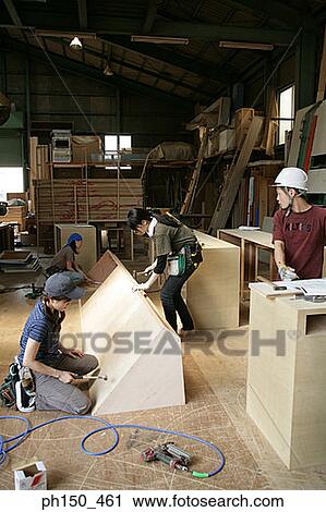 Stock Image - Four carpenters working in a workshop. Fotosearch