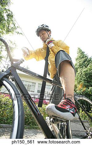 Stock Image - Low angle view of a young man riding a bicycle and talking on a walky talky. Fotosearch