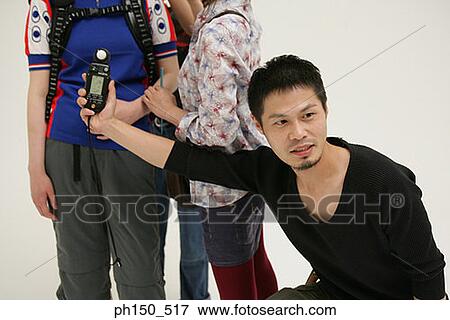 Stock Photo - Photographer using a light meter in front of a female fashion model. Fotosearch