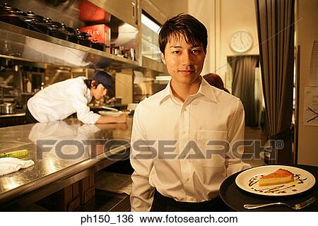 Portrait of a waiter holding a plate of food with a chef talking to a waitress in the background View Large Photo Image Stock Photograph - Portrait of a waiter holding a plate of food with a chef talking to a waitress in the background. Fotosearch