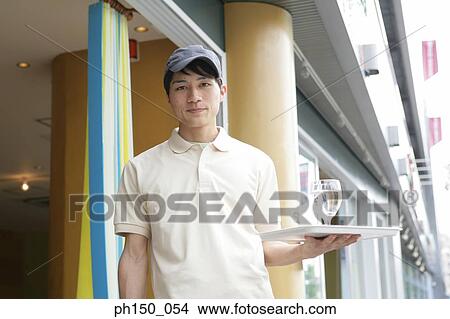 Portrait of a waiter holding a tray with a glass of water in front of a restaurant View Large Photo Image Picture - Portrait of a waiter holding a tray with a glass of water in front of a restaurant. Fotosearch