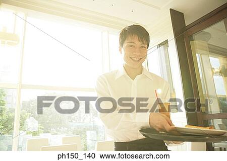 Portrait of a waiter standing and holding a tray View Large Photo Image Stock Image - Portrait of a waiter standing and holding a tray. Fotosearch