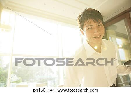 Portrait of a waiter standing and holding a tray View Large Photo Image Stock Image - Portrait of a waiter standing and holding a tray. Fotosearch
