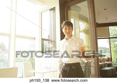 Portrait of a waiter standing and holding a tray View Large Photo Image Stock Photo - Portrait of a waiter standing and holding a tray. Fotosearch