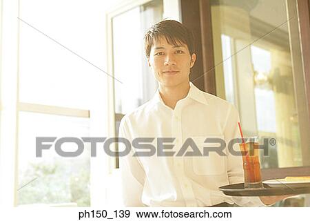 Portrait of a waiter standing and holding a tray View Large Photo Image Stock Photo - Portrait of a waiter standing and holding a tray. Fotosearch