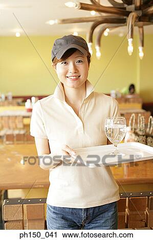 Stock Image - Portrait of a waitress holding a tray with a glass of water and smiling. Fotosearch