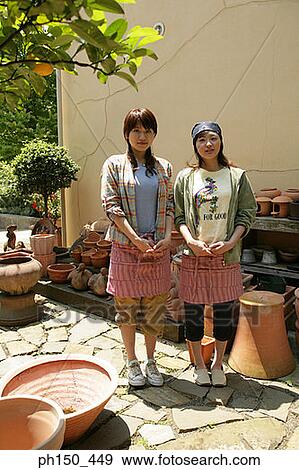 Stock Photo - Portrait of two young women standing in front of flower pots. Fotosearch