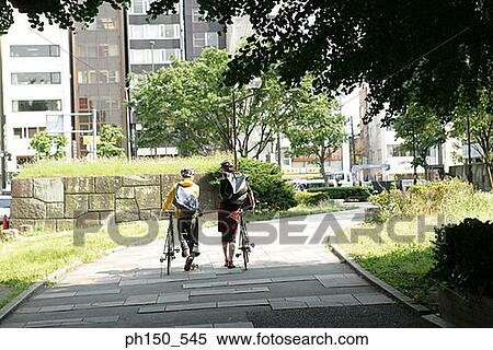 Rear view of a man and a woman walking with bicycles View Large Photo Image Stock Photography - Rear view of a man and a woman walking with bicycles. Fotosearch