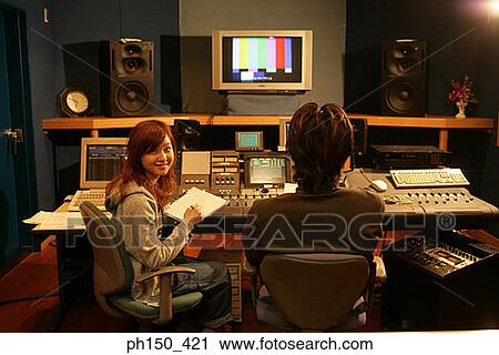 Stock Image - Rear view of a young woman and a man sitting in a recording studio. Fotosearch