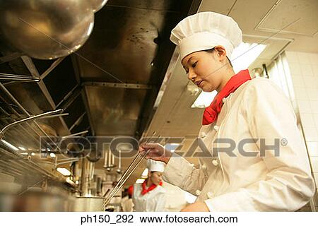 Stock Image - Side profile of a female chef cooking in the kitchen. Fotosearch