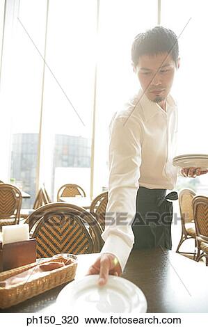 Stock Image - Side profile of a waiter putting plates on the table. Fotosearch