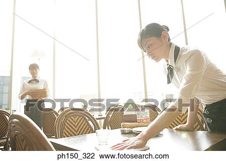 Stock Image - Side profile of a waitress setting a table in a restaurant. Fotosearch
