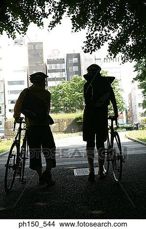 Silhouette of two people standing with bicycles View Large Photo Image Picture - Silhouette of two people standing with bicycles. Fotosearch