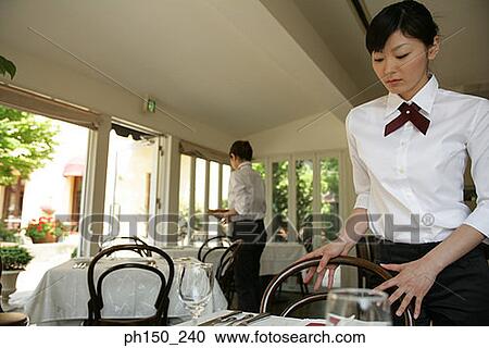 Waitress arranging chair along a table in a restaurant View Large Photo Image Stock Image - Waitress arranging chair along a table in a restaurant. Fotosearch