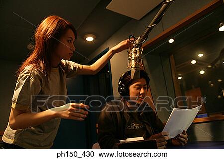 Young woman holding a microphone over a young man recording music in a recording studio View Large Photo Image Stock Image - Young woman holding a microphone over a young man recording music in a recording studio. Fotosearch
