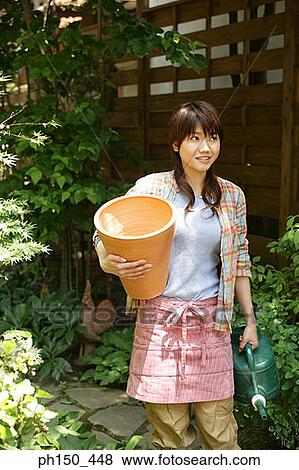 Young woman holding a vase and a watering can in a plant nursery View Large Photo Image Stock Photo - Young woman holding a vase and a watering can in a plant nursery. Fotosearch