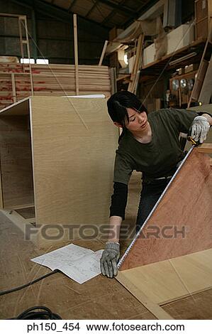 Picture - Young woman measuring a sheet of plywood with a tape measure. Fotosearch