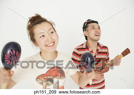 Stock Photo - Close-up of a young woman holding maracas with a young man playing a toy guitar. Fotosearch