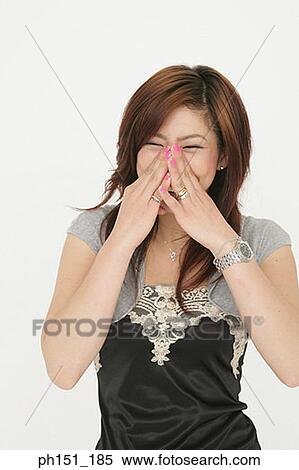 Stock Photography - Close-up of a young woman smiling with her hand over her mouth. Fotosearch