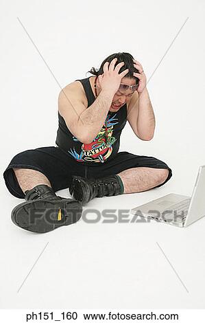 Mid adult man sitting in front of a laptop with his hands on his head and gritting his teeth View Large Photo Image Stock Image - Mid adult man sitting in front of a laptop with his hands on his head and gritting his teeth. Fotosearch
