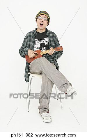 Portrait of a young man sitting on a chair and playing the guitar View Large Photo Image Stock Image - Portrait of a young man sitting on a chair and playing the guitar. Fotosearch